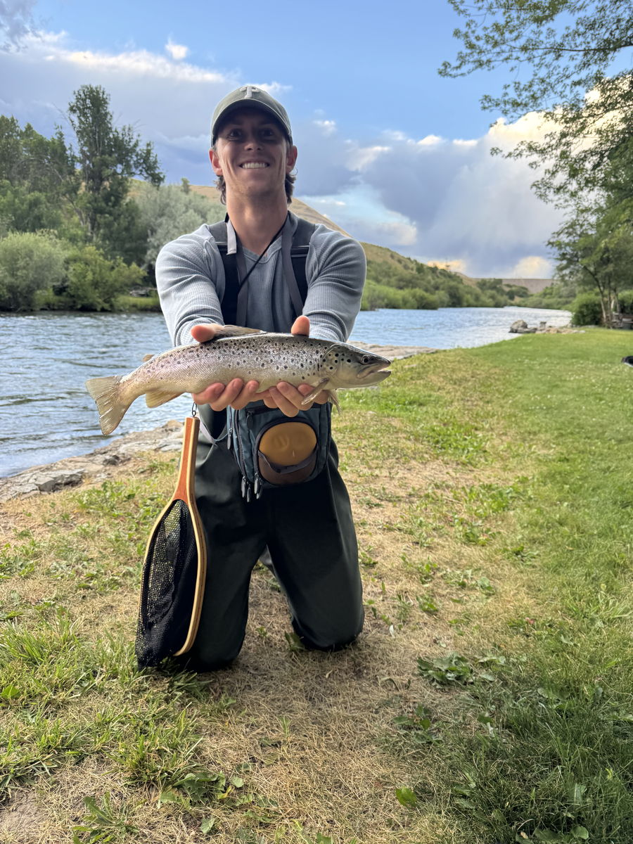 Tanner Hale holding a trout while fly fishing by a river